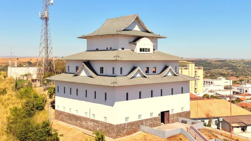 Prédio branco em estilo de castelo japonês no alto de uma colina em Assaí, Paraná, com a cidade ao fundo