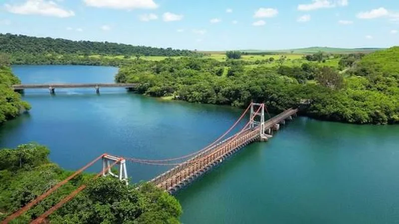 Vista aérea de uma ponte pênsil vermelha sobre o rio, cercada de mata, em Chavantes, SP