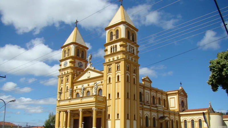 Fachada amarela da Catedral de Jacarezinho, com duas torres, em dia de céu azul